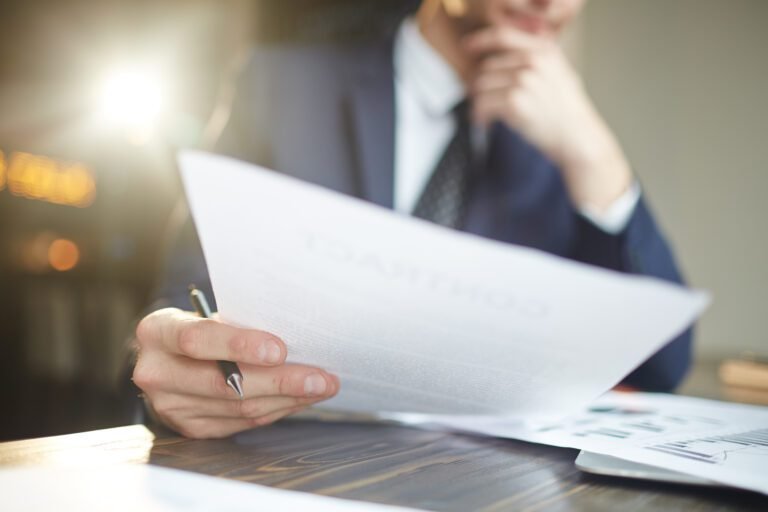 Closeup portrait of unrecognizable successful businessman wearing black formal suit analyzing documents and finance statistics at desk, thinking