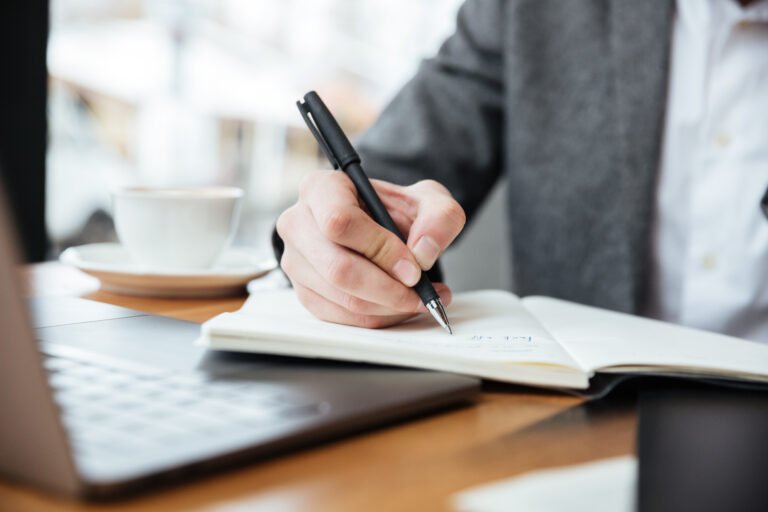 Cropped image of business man sitting by the table in cafe with laptop computer and writing something